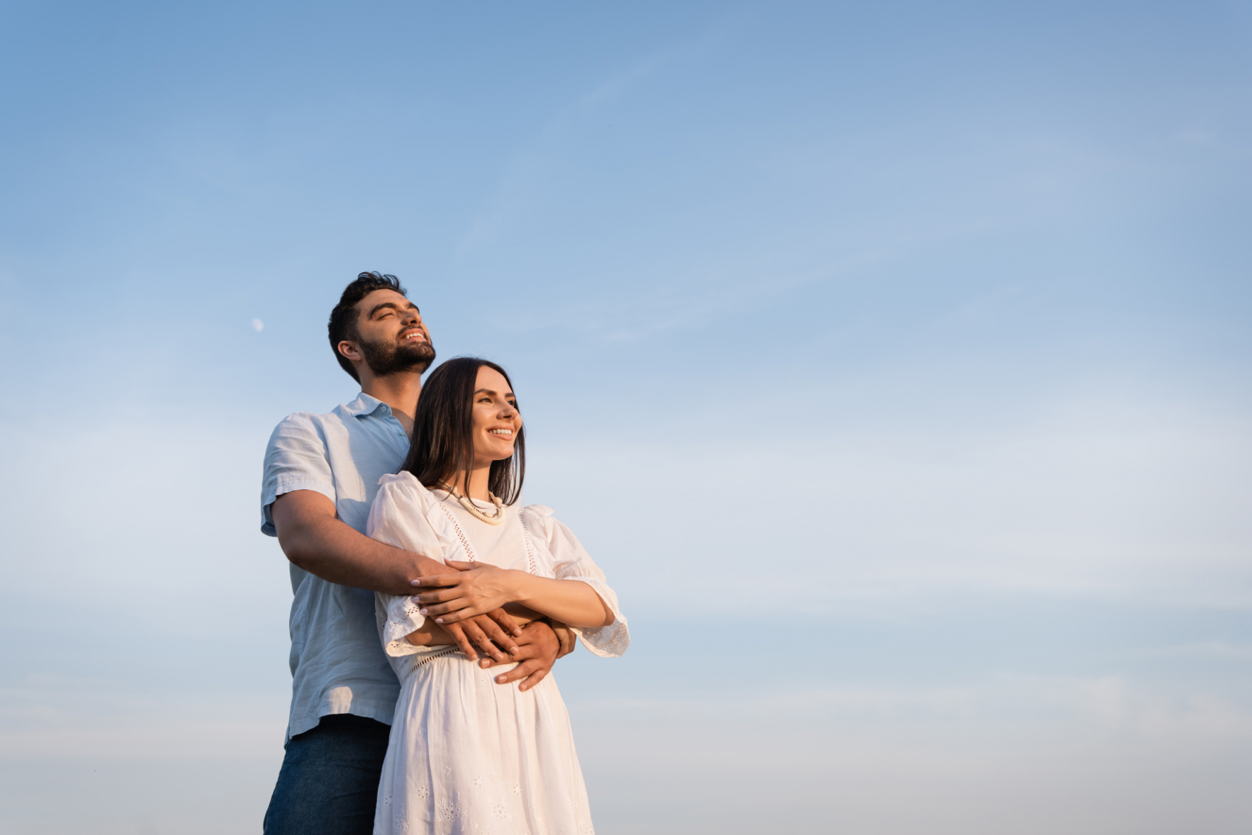 bearded man embracing happy woman in white dress while looking a photo of couple contemplating having a baby
