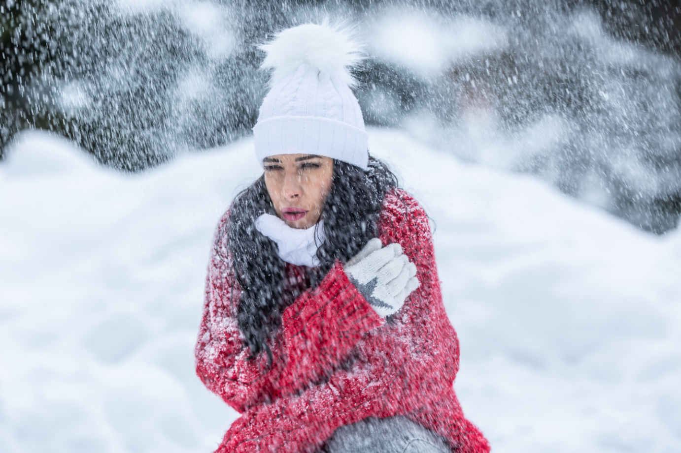 Woman is shaking from cold during windy snowy winter day outdoors despite wearing warm clothes. Photo of woman in cold winter