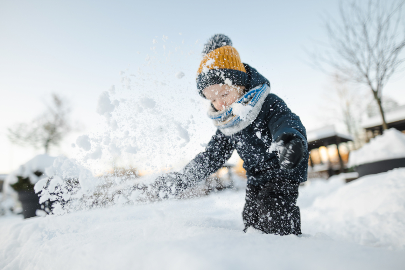 Adorable toddler boy having fun in a city on snowy winter day. Cute child wearing warm clothes playing in a snow.