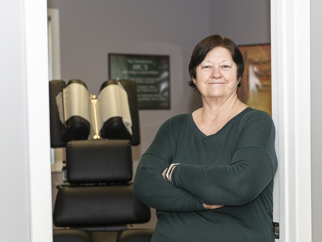 Dr sharon Smiling woman with arms crossed standing in doorway, green sweater, in a clinic or salon setting.