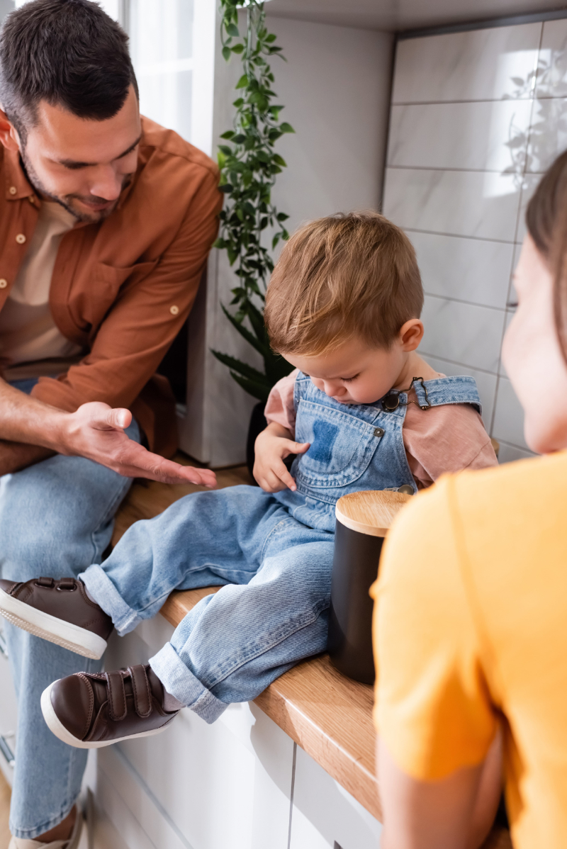 Toddler boy sitting on kitchen worktop near parents at home Father and young son sharing a quiet moment together in a warm family kitchen