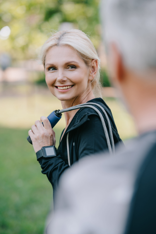 selective focus of smiling sportsman with jump rope looking at mature sportsman active woman 50s lifestyle