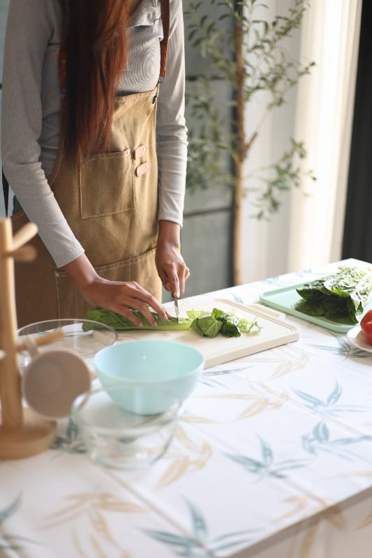 A woman in an apron preparing a fresh salad on the table in kitchen.